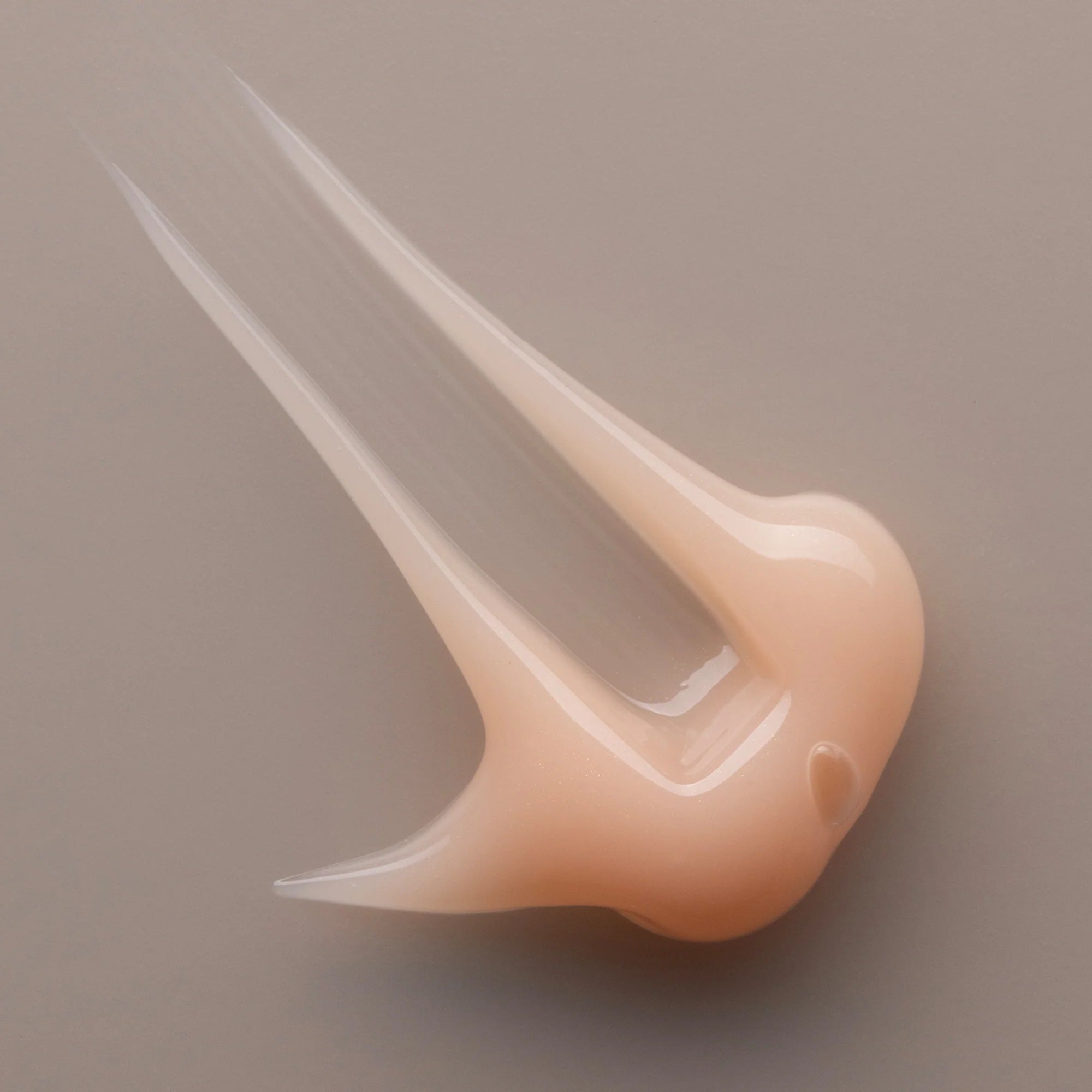 Close-up of a beige nail tip with a clear gel of Antipodes Baptise cream on a brown background