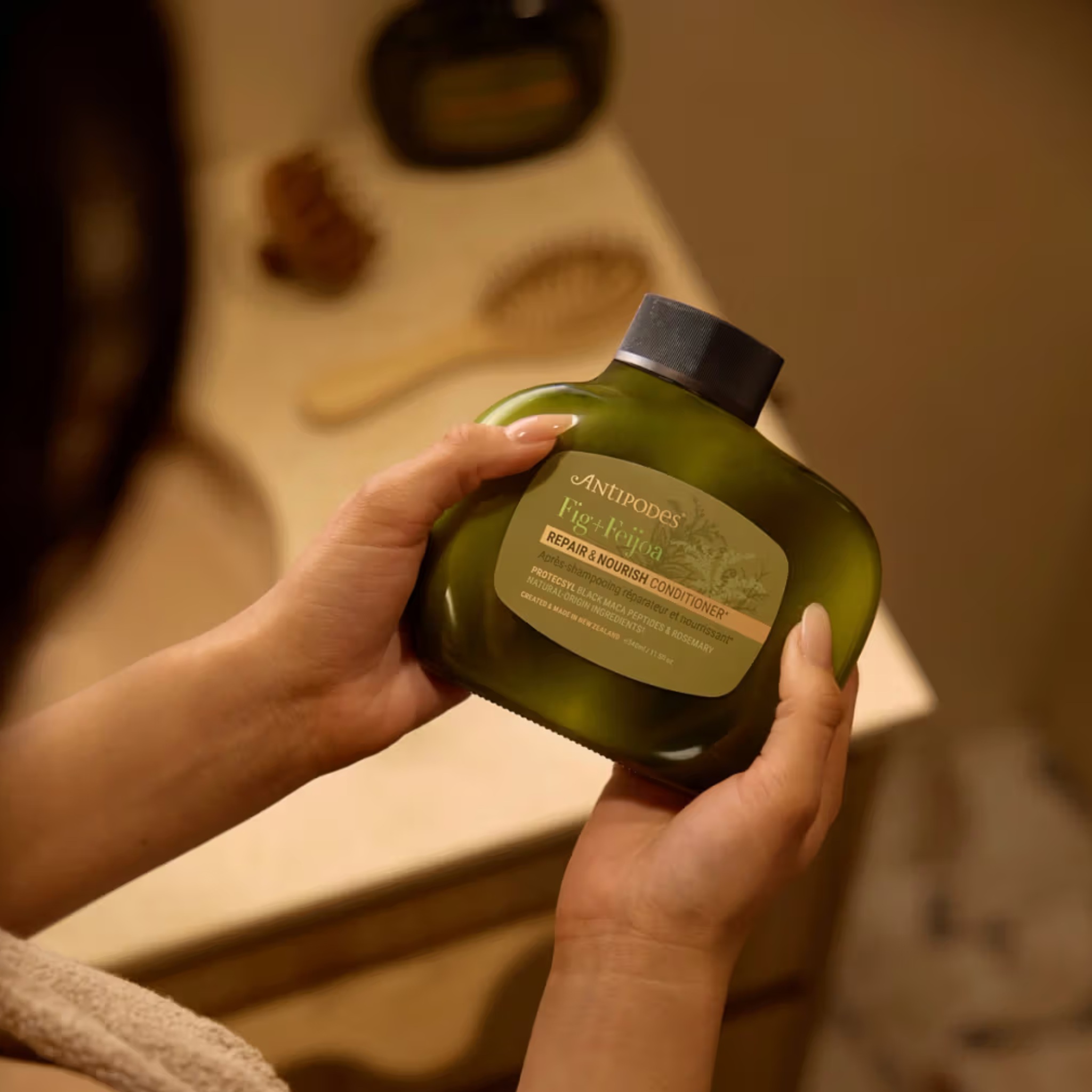 Person holding a green bottle of Antipodes fig and feijoa shampoo product in a bathroom setting.