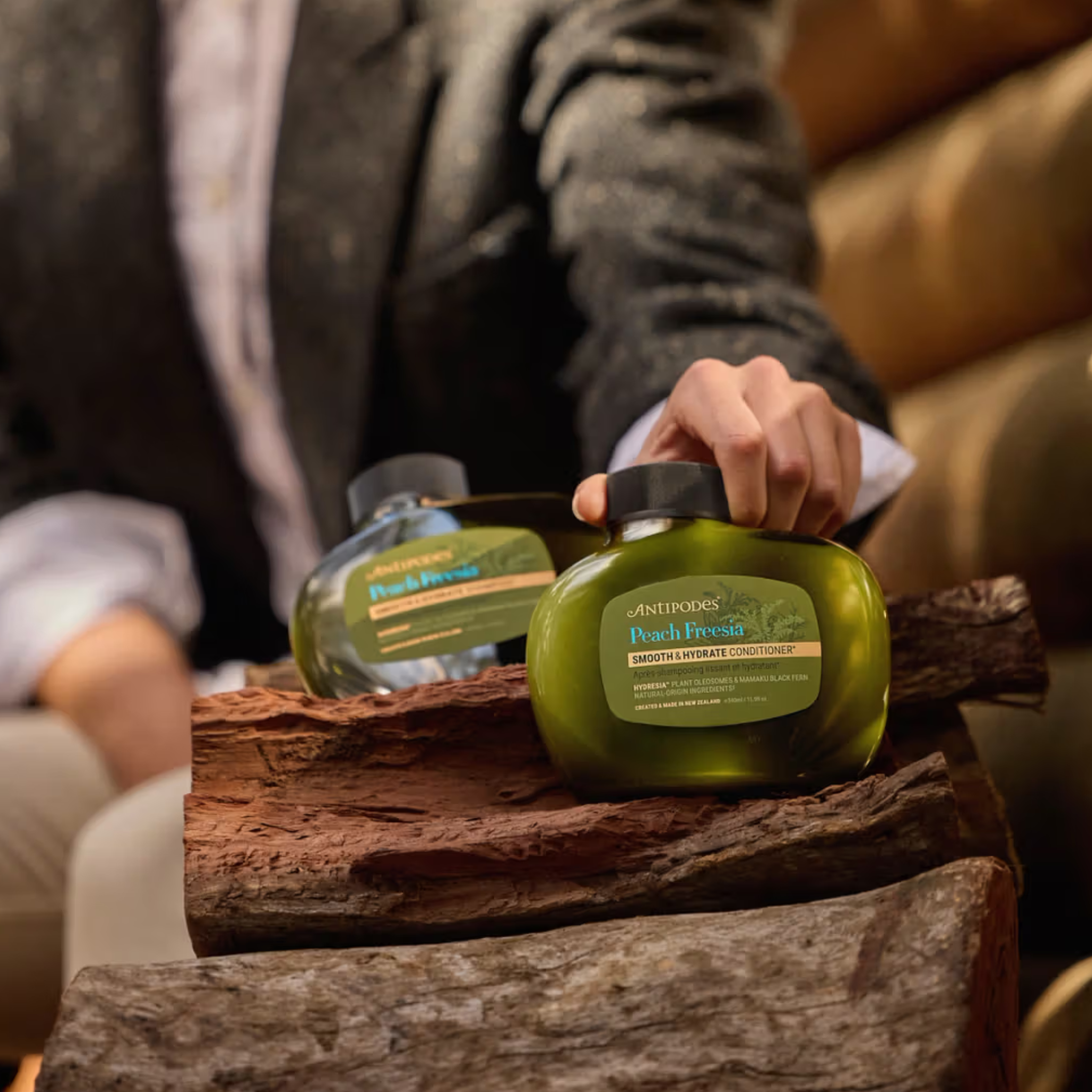 Person holding a bottle of Antipodes Peach Fresh Conditioner on a wooden surface.