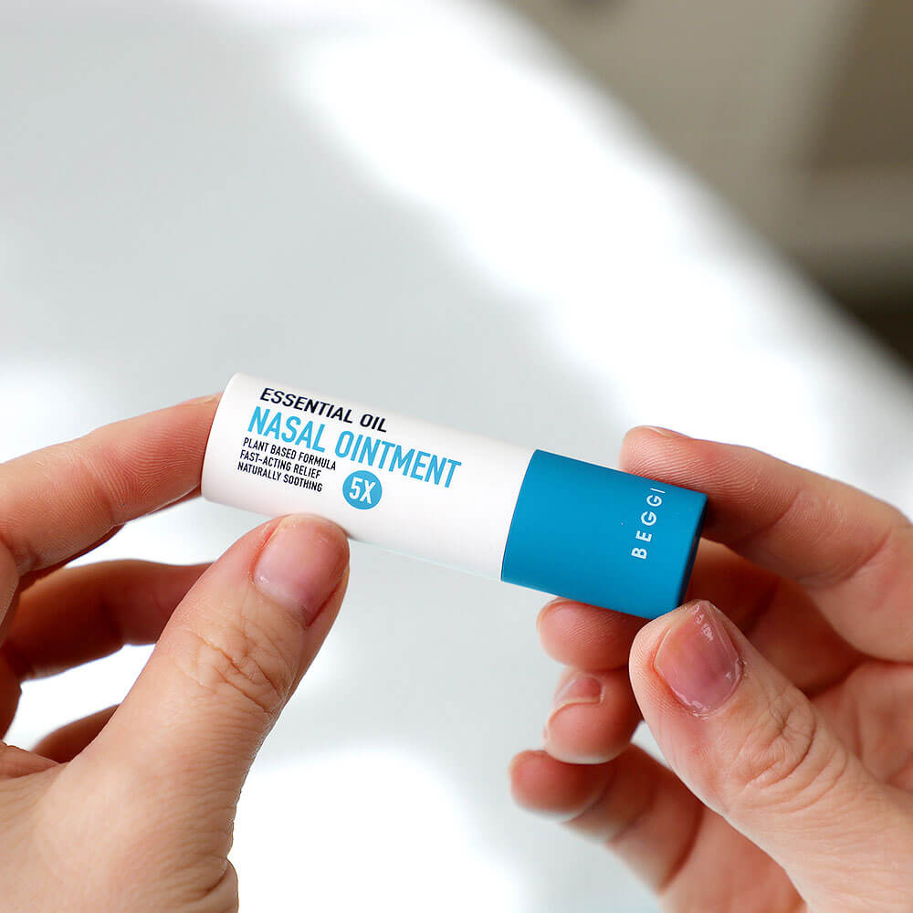 Hand holding a small container of nasal ointment with a blue and white design.