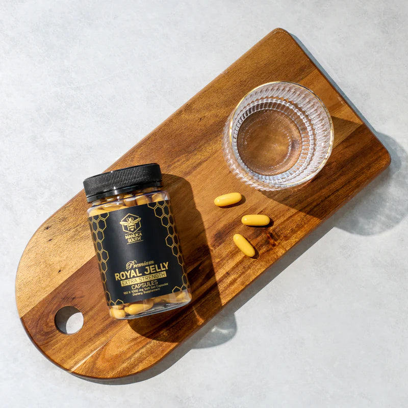 Jar of Royal Jelly capsules on a wooden cutting board with scattered capsules.