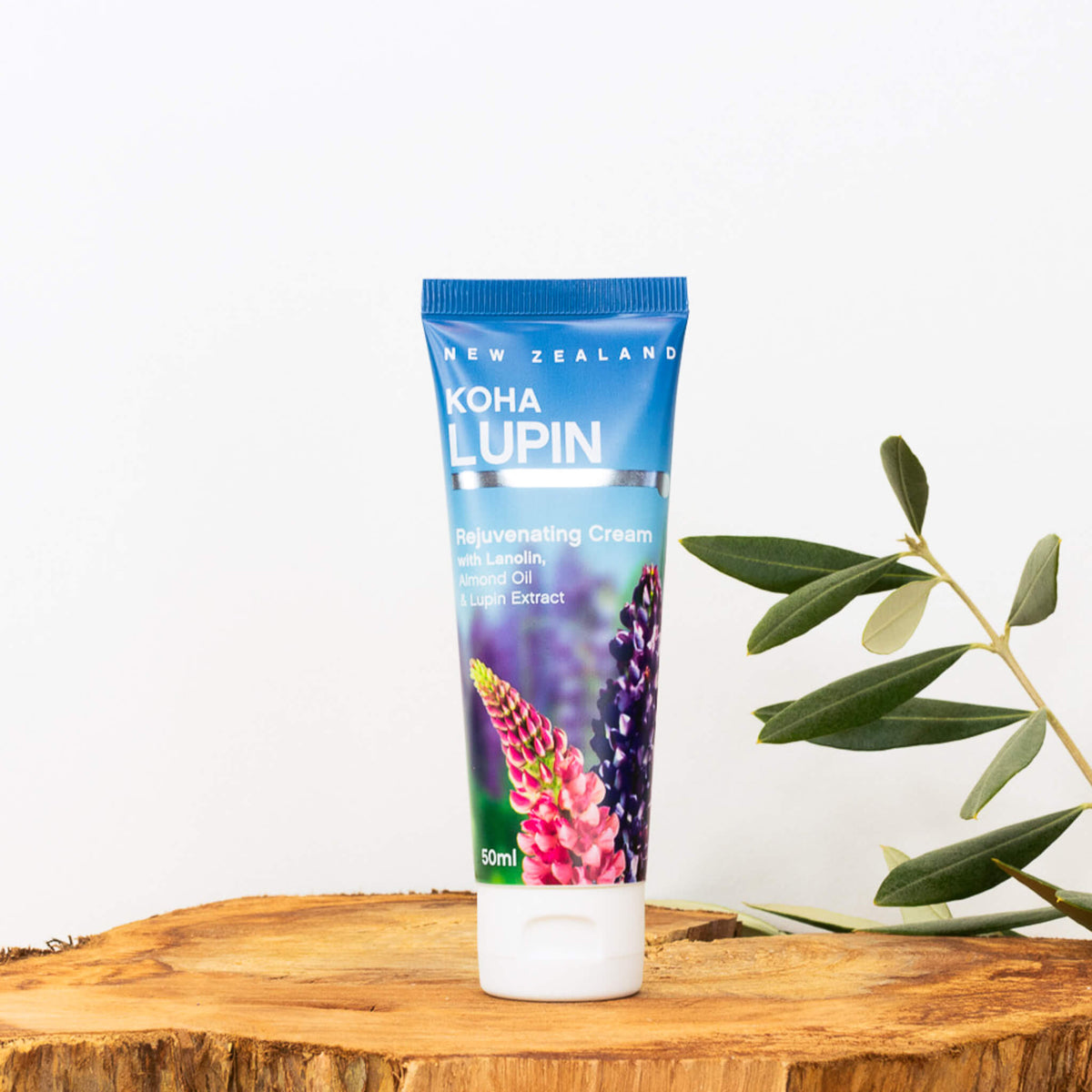 A tube of KOUA LUPIN Rejuvenating Cream 50ml with a colorful design, placed on a wooden surface with a white background and some green leaves in the background.