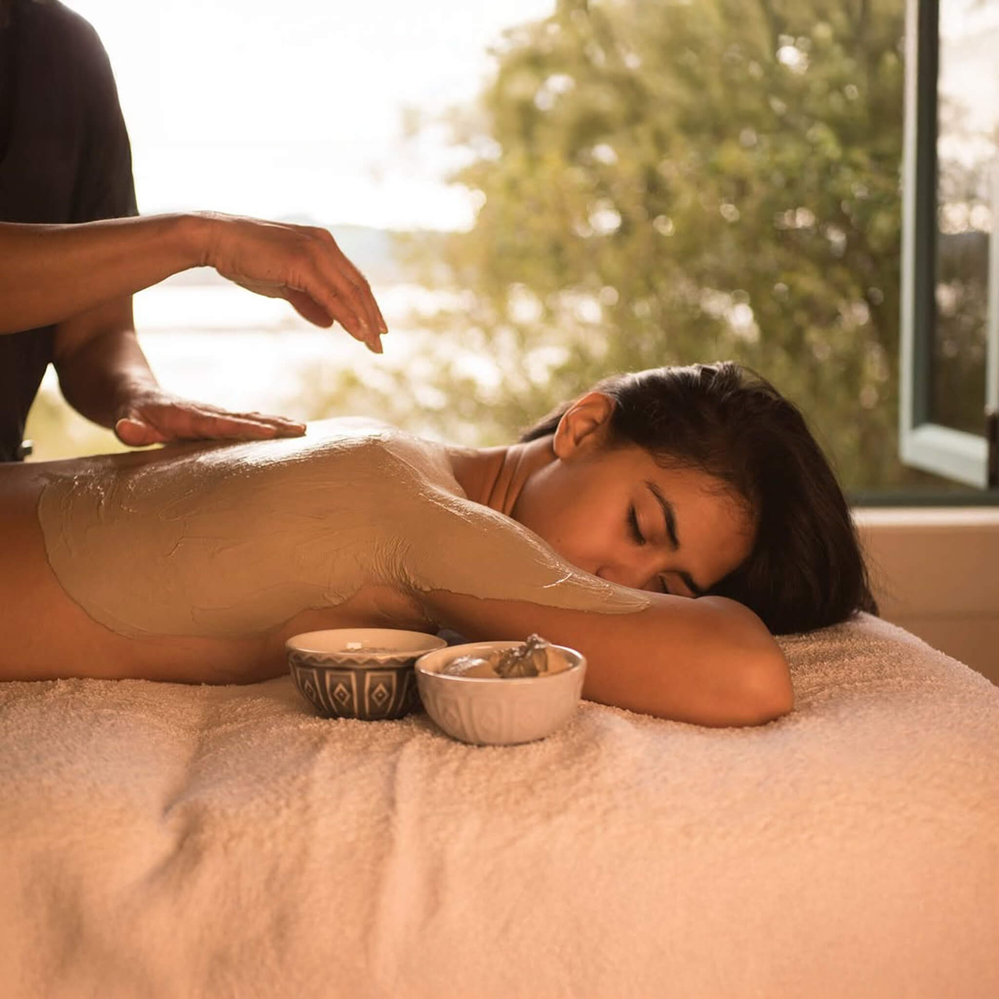 Woman receiving a Puresource Rotorua Thermal Mud Mask with a serene background