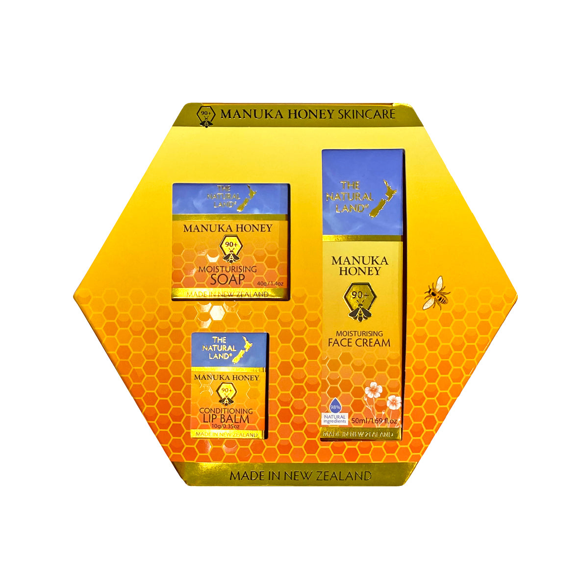 A hexagon-shaped The natural Land gift box containing three manuka honey products: a facial cream, a lip balm, and a soap, with labels in yellow and blue colors.
