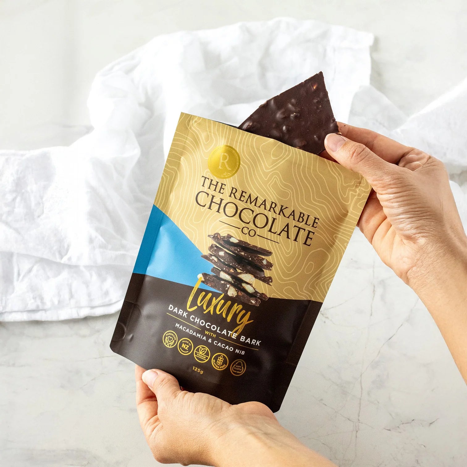 Hand holding a package of The Remarkable Chocolate Co. luxury dark chocolate bark with macadamia.