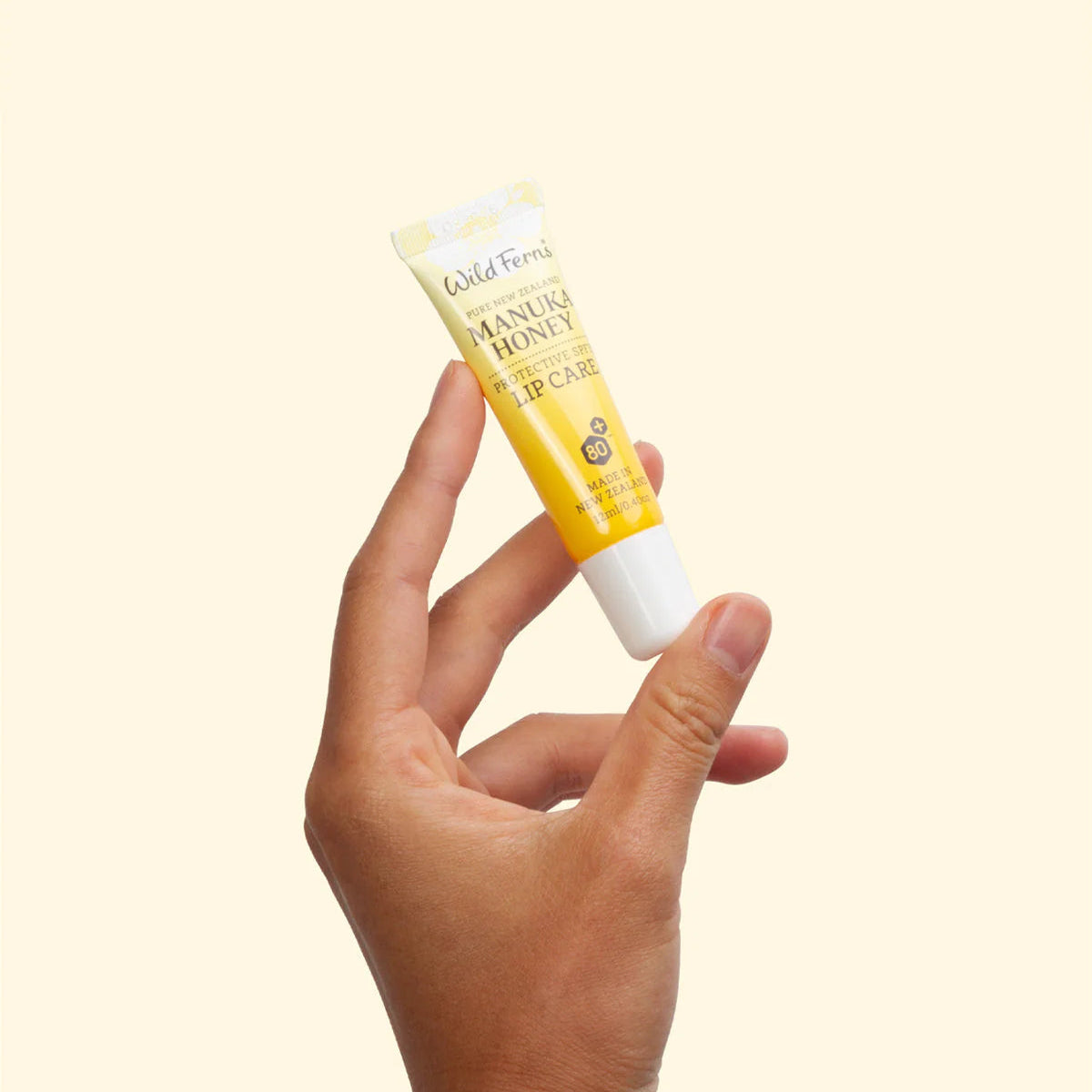 Hand holding a tube of Wild Ferns Manuka Honey lip balm against a light background