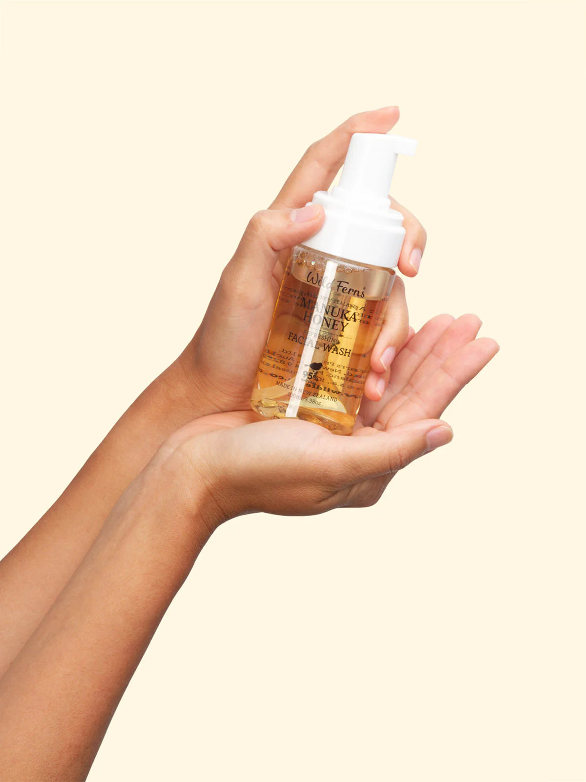 Hand holding a bottle of Wild Fenn's Manuka Honey Face wash against a beige background