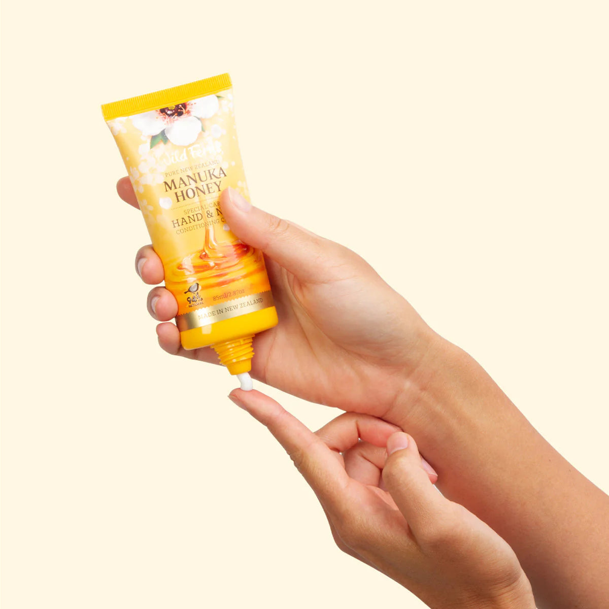 Hand holding a tube of Wild Ferns Manuka Honey Hand and Nail Creme against a beige background