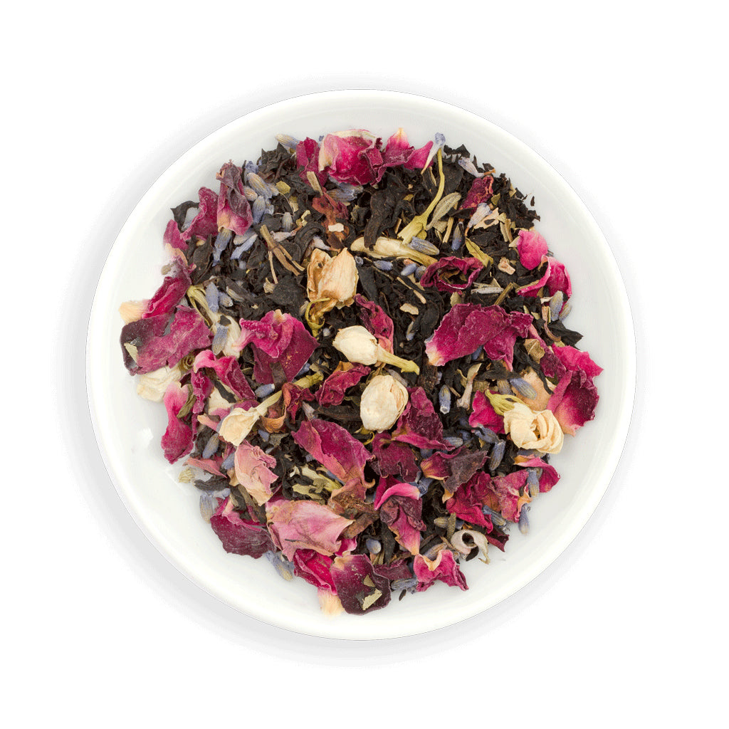 Assorted dried Zealong tea leaves with flowers and herbs in a white bowl on a white background