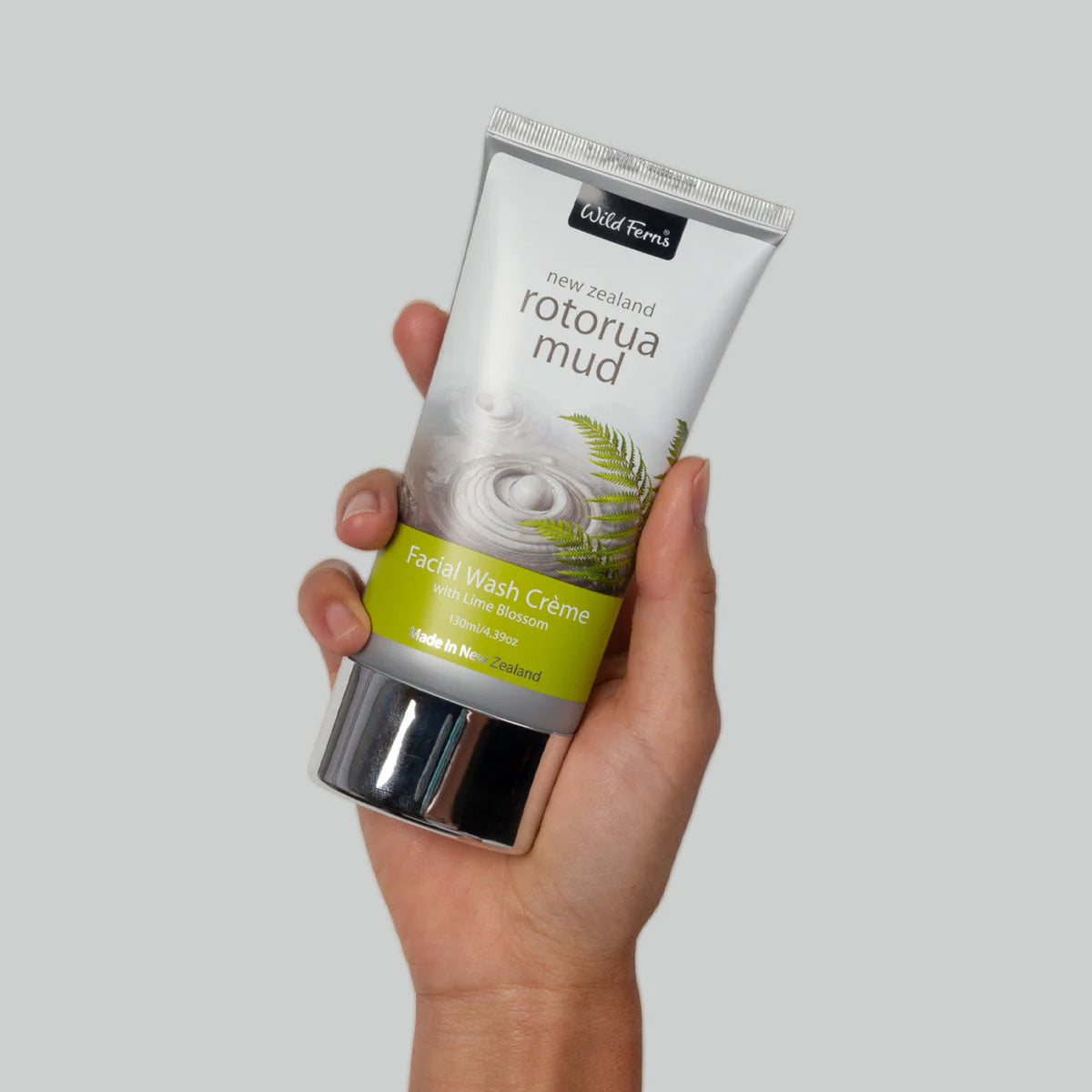 Hand holding a tube of Wild Ferns Rotorda Mud facial wash cream against a gray background