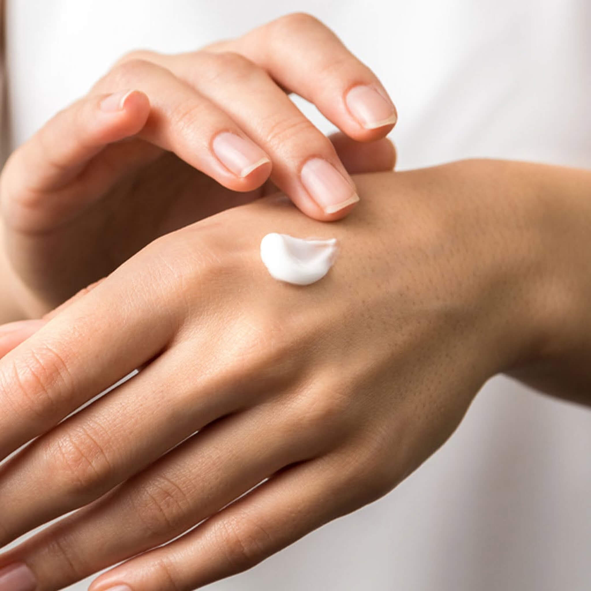 Hand applying Wild Fern's Manuka Honey Hand and Nail cream to another hand with a neutral background