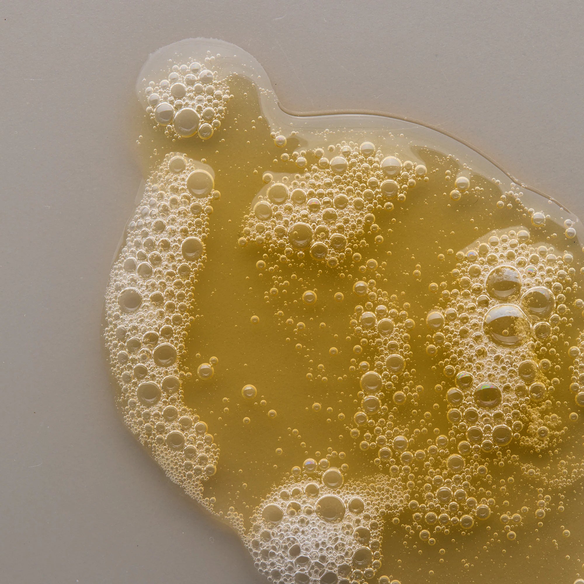 Close-up of a yellow liquid of Antipodes Gospel Gel Cleanser with bubbles on a light gray background