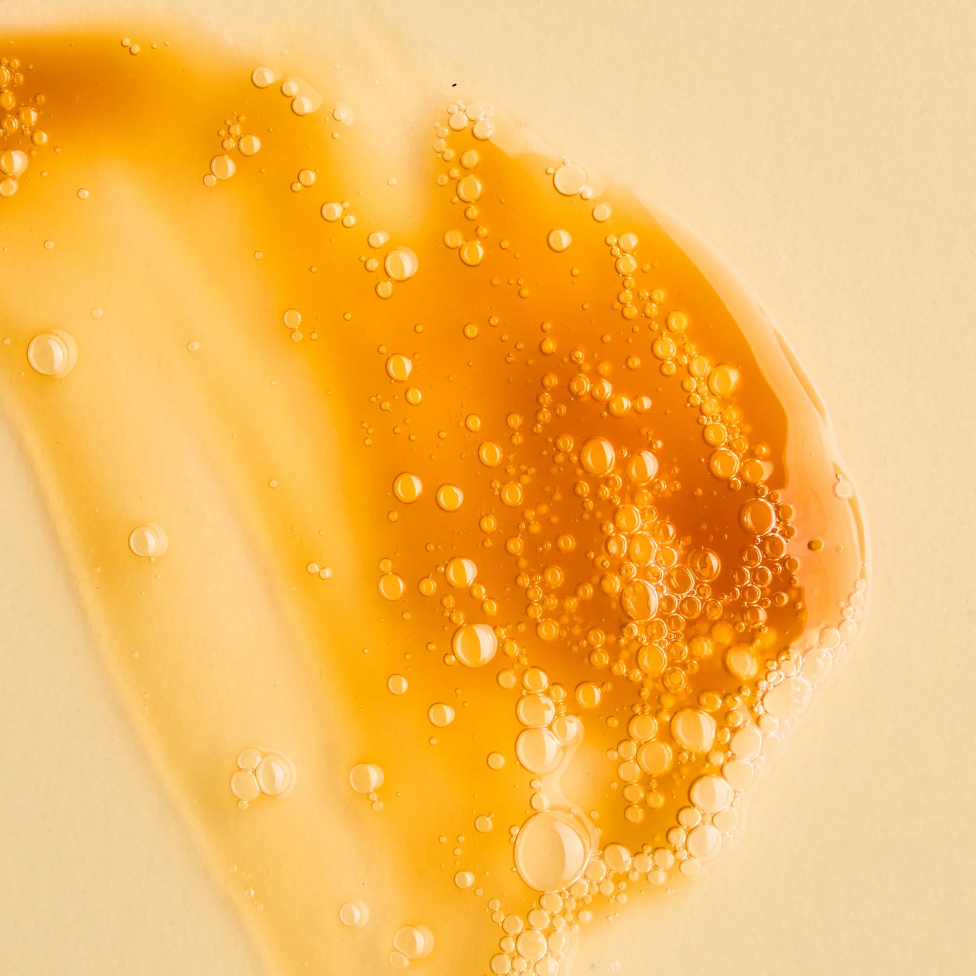 Close-up of orange liquid with bubbles of Antipodes Juliet cleanser on a beige background
