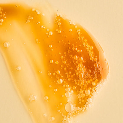 Close-up of orange liquid with bubbles of Antipodes Juliet cleanser on a beige background