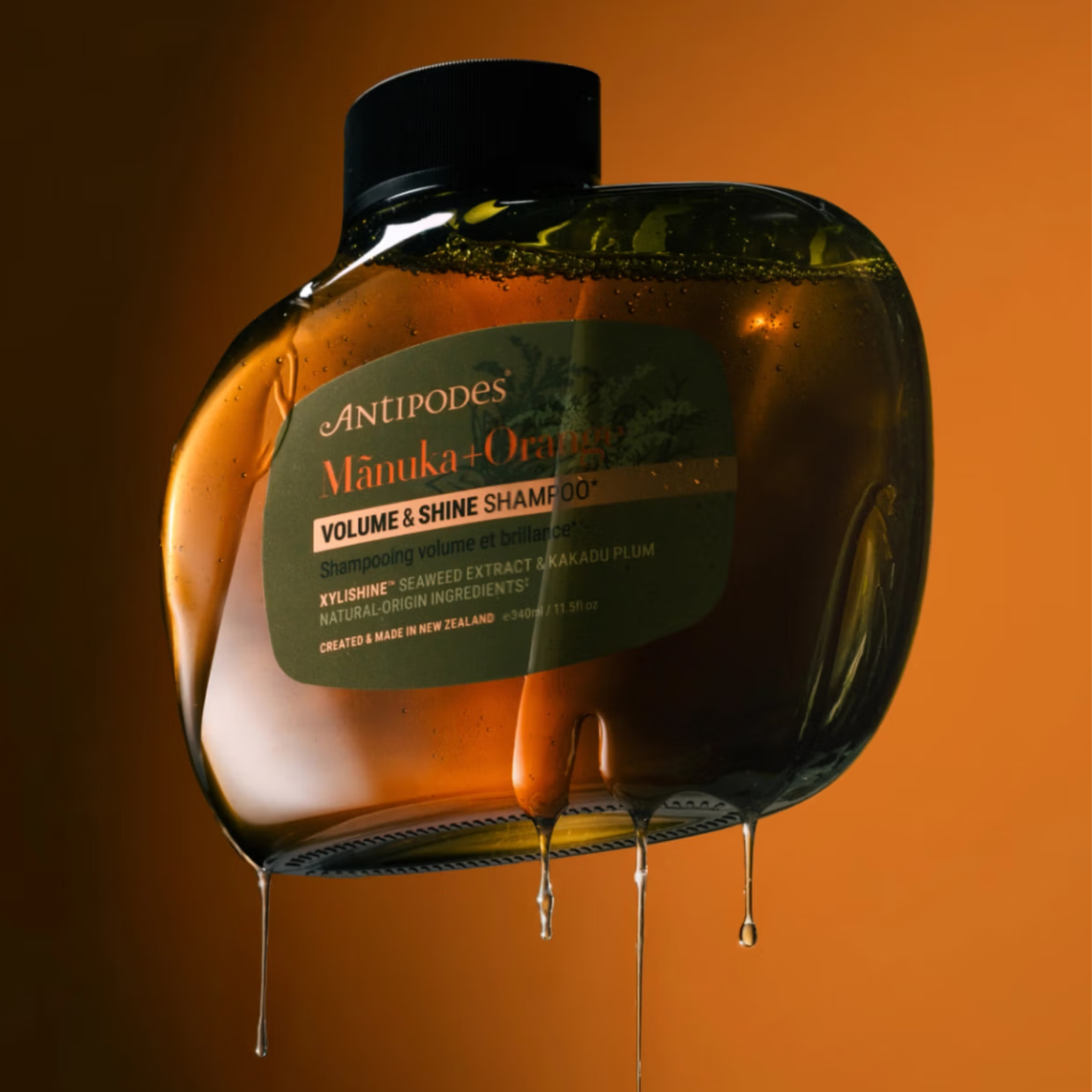 Anipodes Manuka Orange Volume & Shine Shampoo bottle with droplets on an orange background