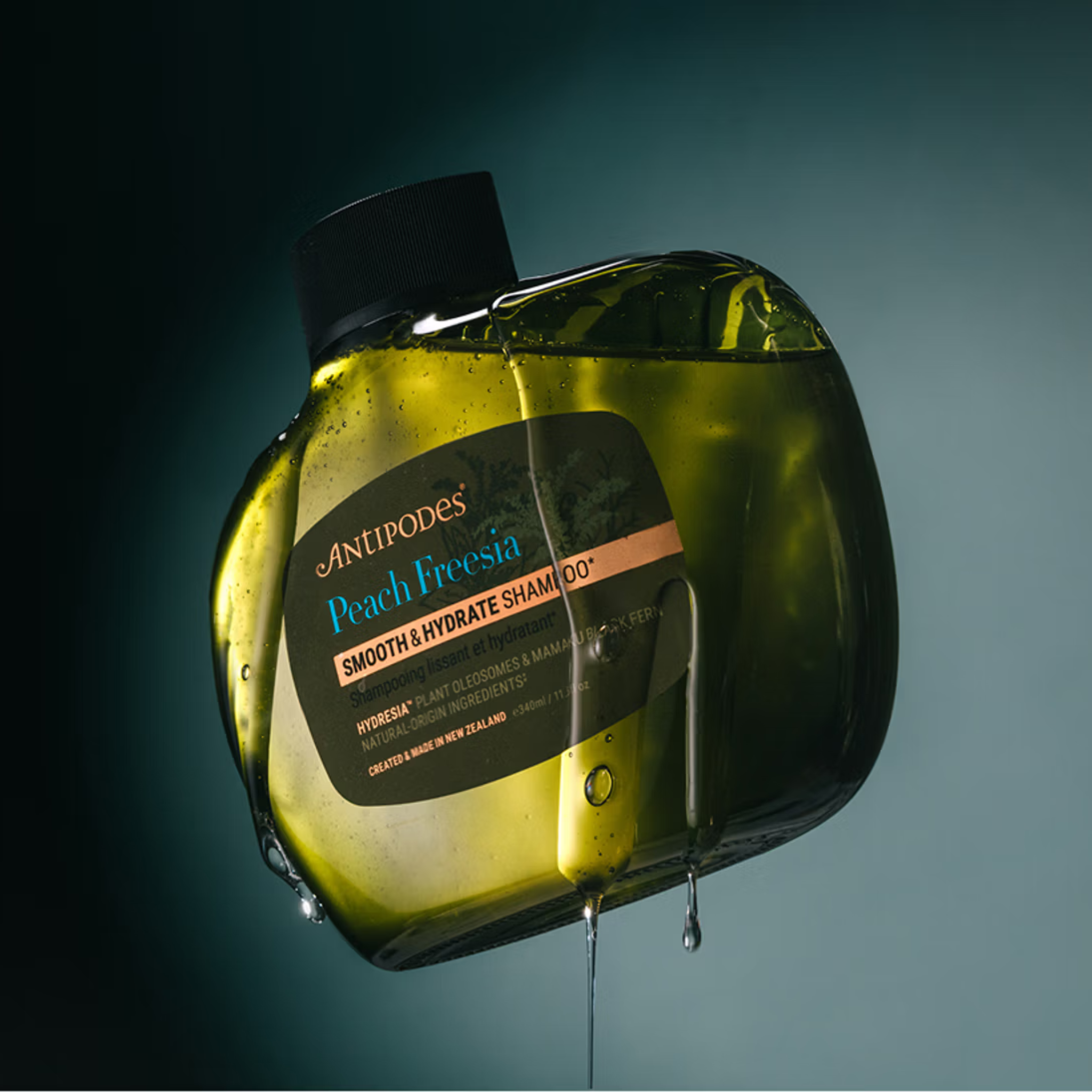 Antipodes Peach Freesia shampoo bottle with liquid dripping, on a dark background