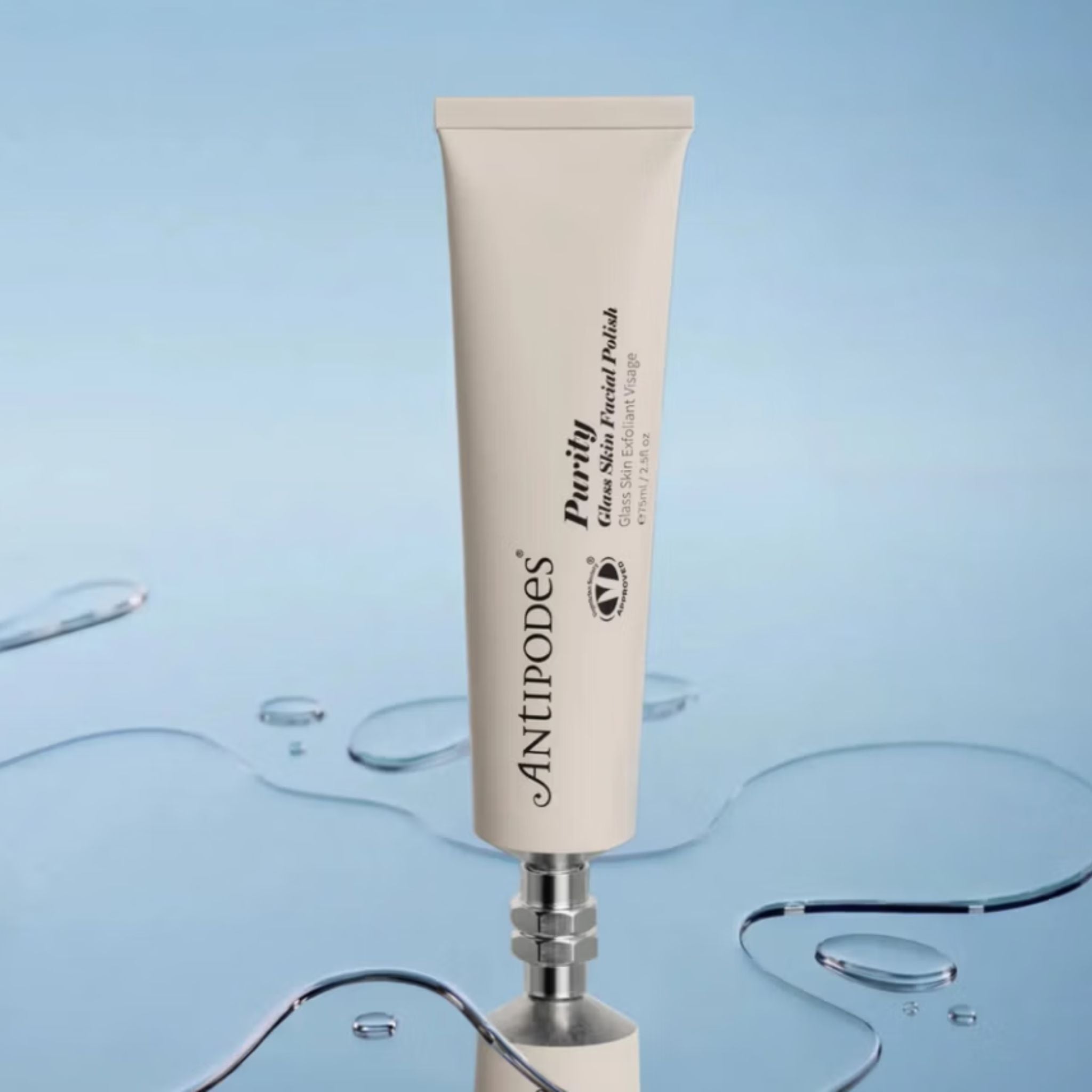 A single tube of Antipodes Purify Gloss Shine Facial Polish stands upright on a metallic stand against a light blue background with water droplets and curved transparent lines.