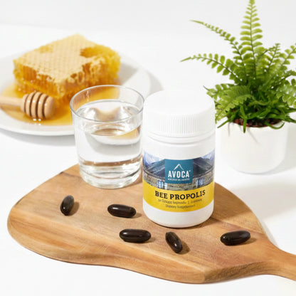 Avoca Bee Propolis supplement bottle on a wooden board with honey, honeycomb, and a glass of water.