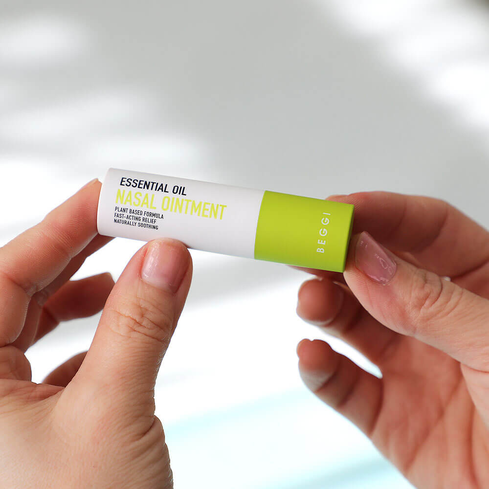 Hand holding a tube of essential oil nasal ointment against a light background