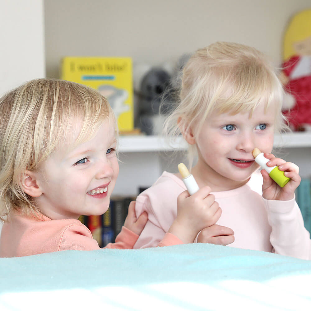 Two young girls playing with makeup products in a room with books and toys.