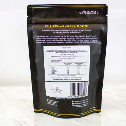 Back view of a resealable stand-up pouch of coffee on a light marble surface. The black pouch has yellow text and borders, with a large white ingredient panel in the center and a barcode near the bottom.
