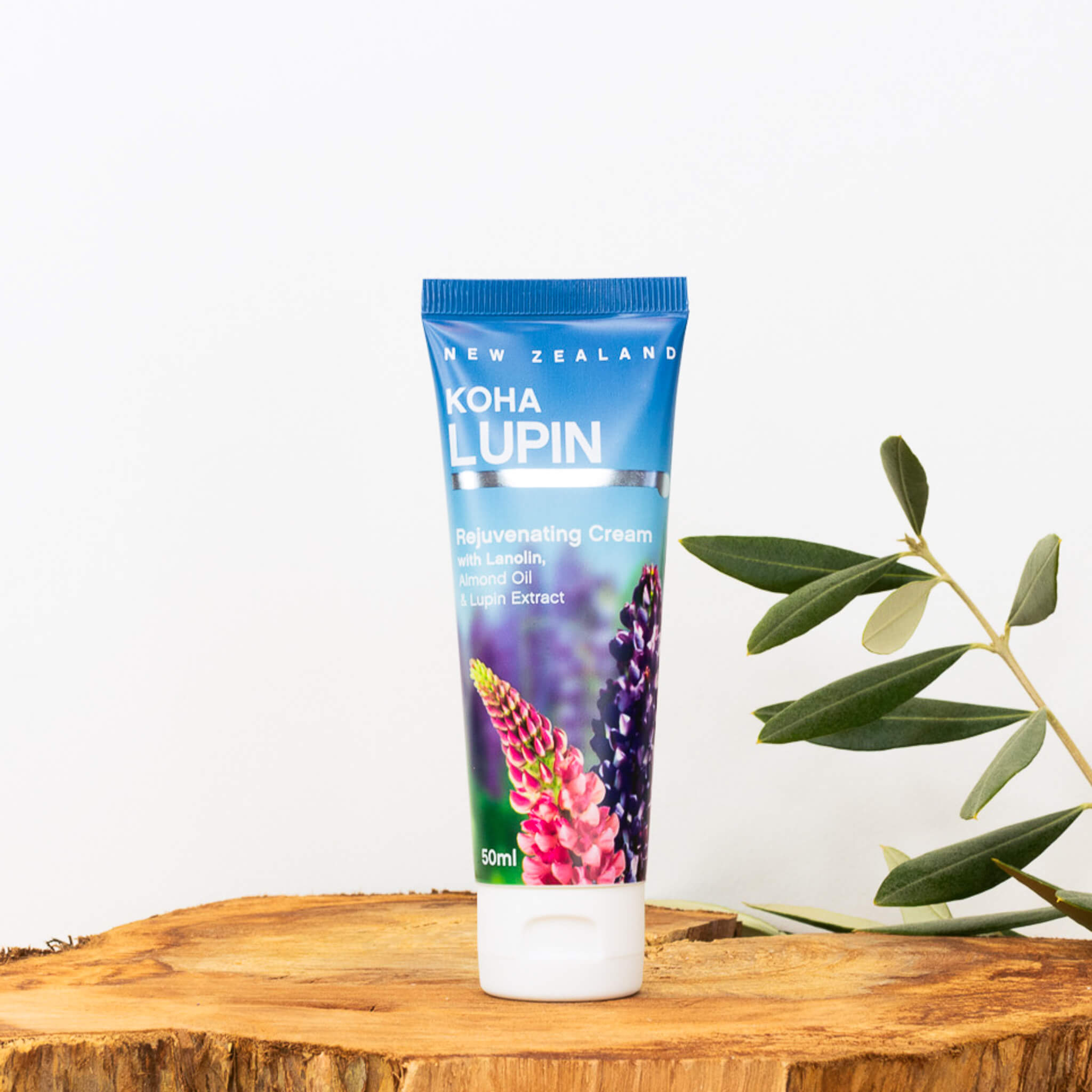A tube of KOUA LUPIN Rejuvenating Cream 50ml with a colorful design, placed on a wooden surface with a white background and some green leaves in the background.