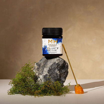 M&H Manuka Honey UMF5+ 250g jar with honey dripper on a stone and moss background