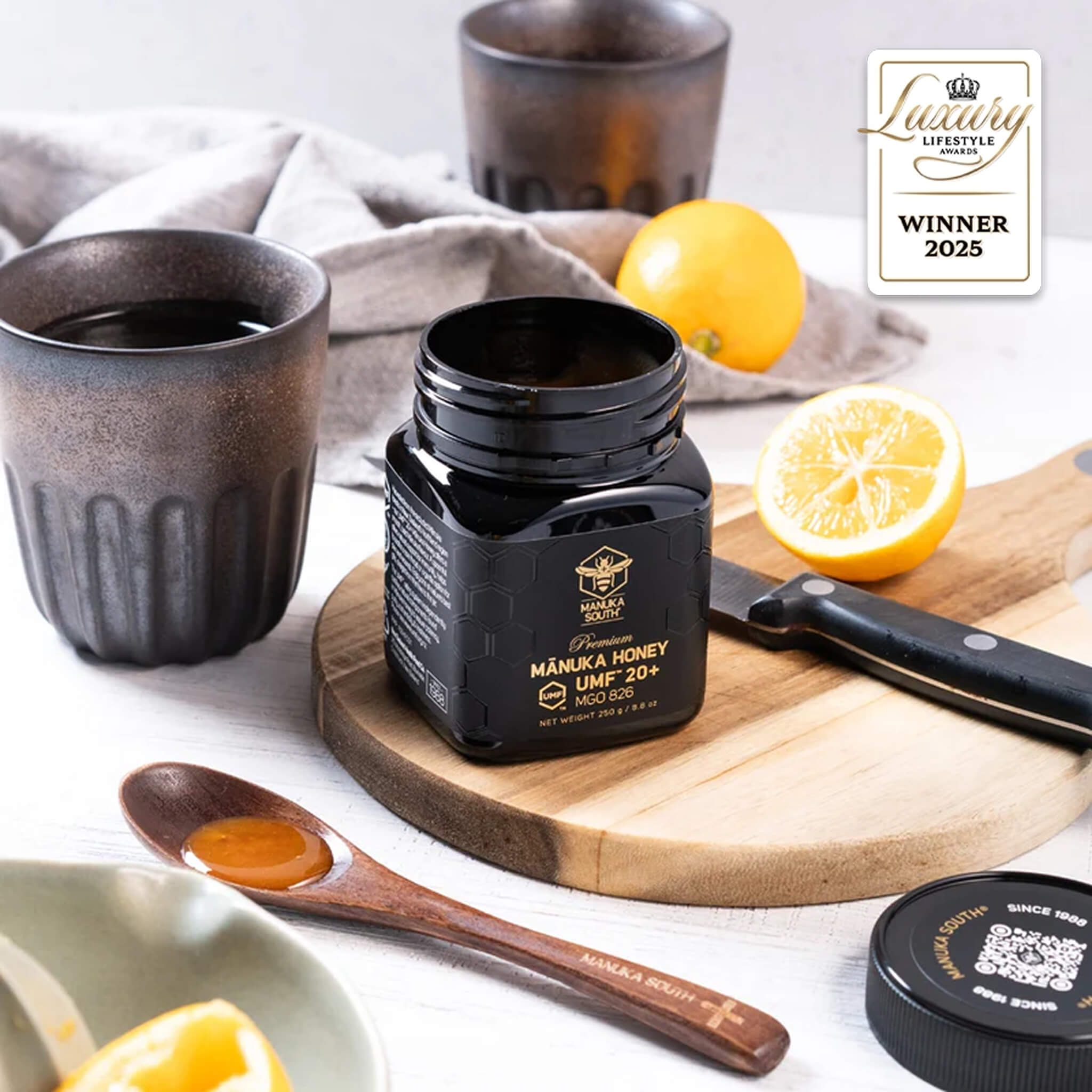 Manuka South Manuka honey UMF 20+ 250g jar with lemons, cups, and a spoon on a wooden board with a 'Lifestyle Award Winner 2025' badge.