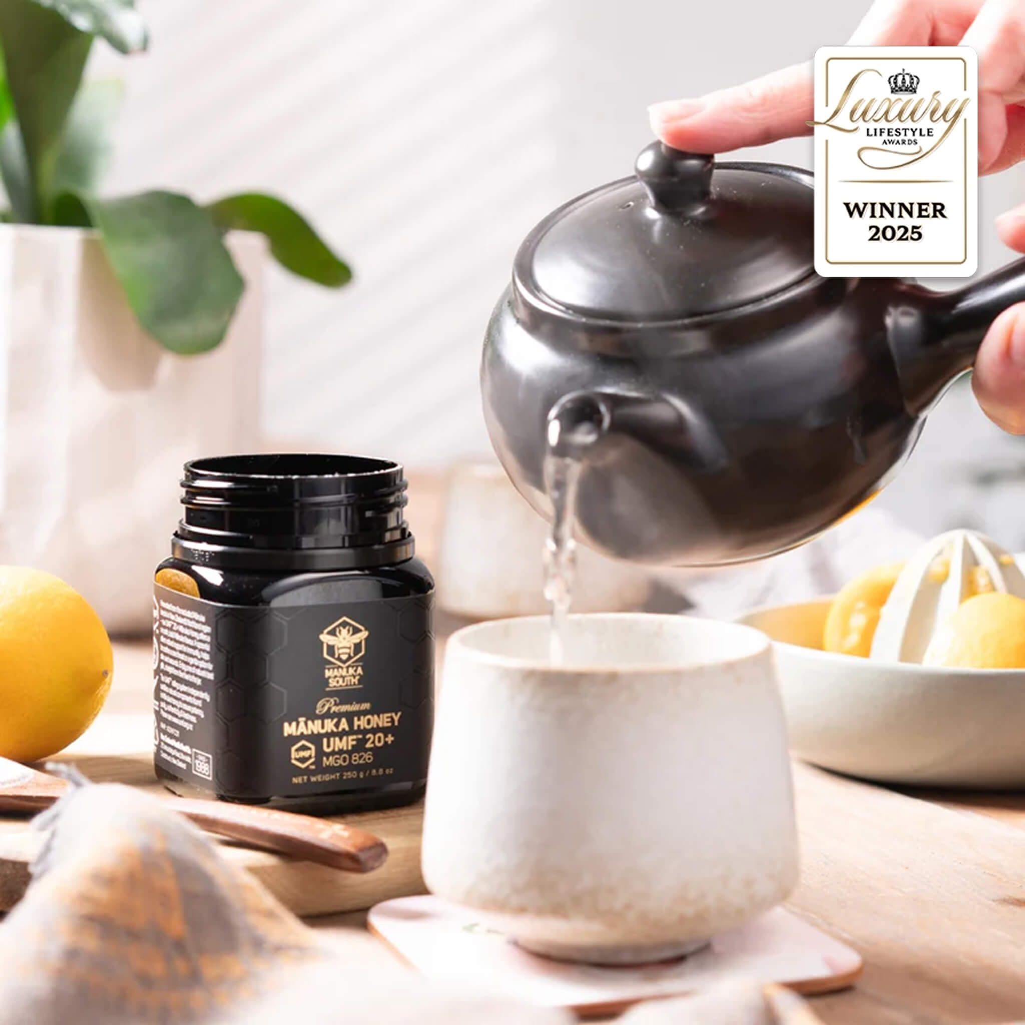 Person pouring tea from a teapot into a cup with Manuka South Manuka Honey UMF 20+ 250g jar on a table.