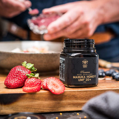 Manuka South Manuka Honey UMF 20+ 250g jar on wooden chopping board with some strawberries