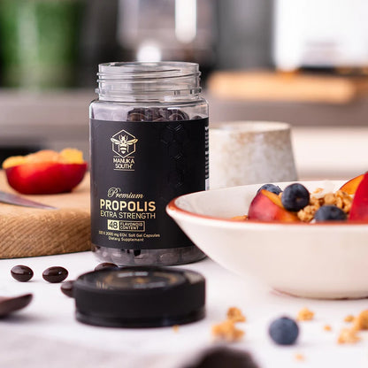Manuka South propolis Soft gel extra strength jar on a table with a bowl of fruit and granola.