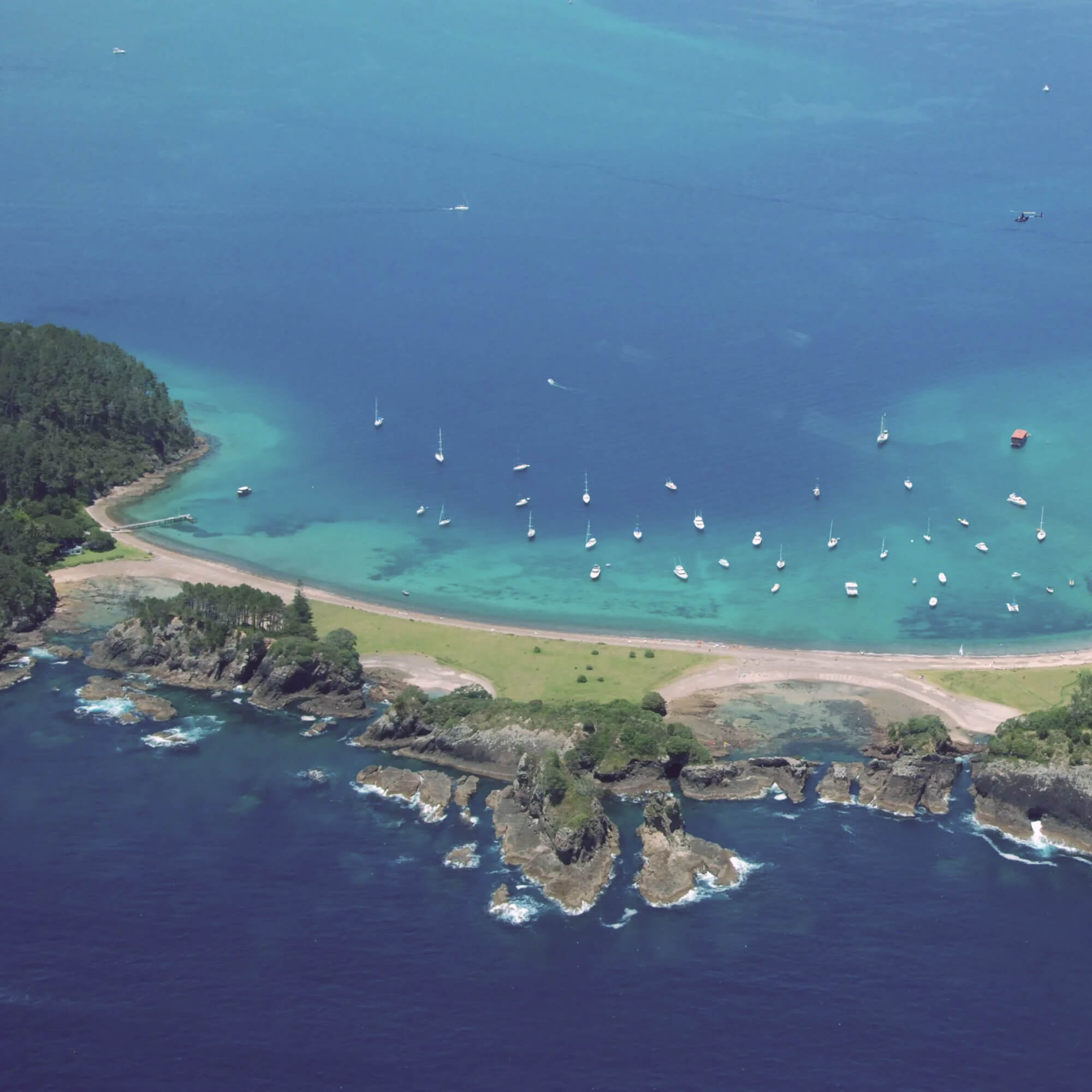 Aerial view of a coastal area of Matauwhi with boats in the water and a grassy strip.