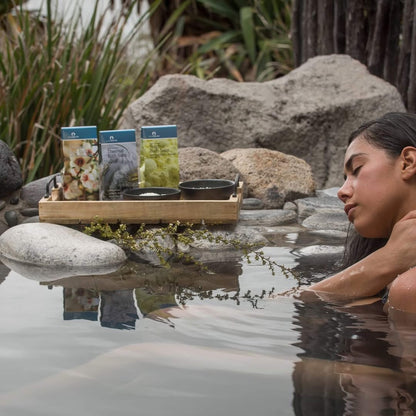 Woman relaxing in a natural hot spring with Puresource bath salts on a rock shelf.