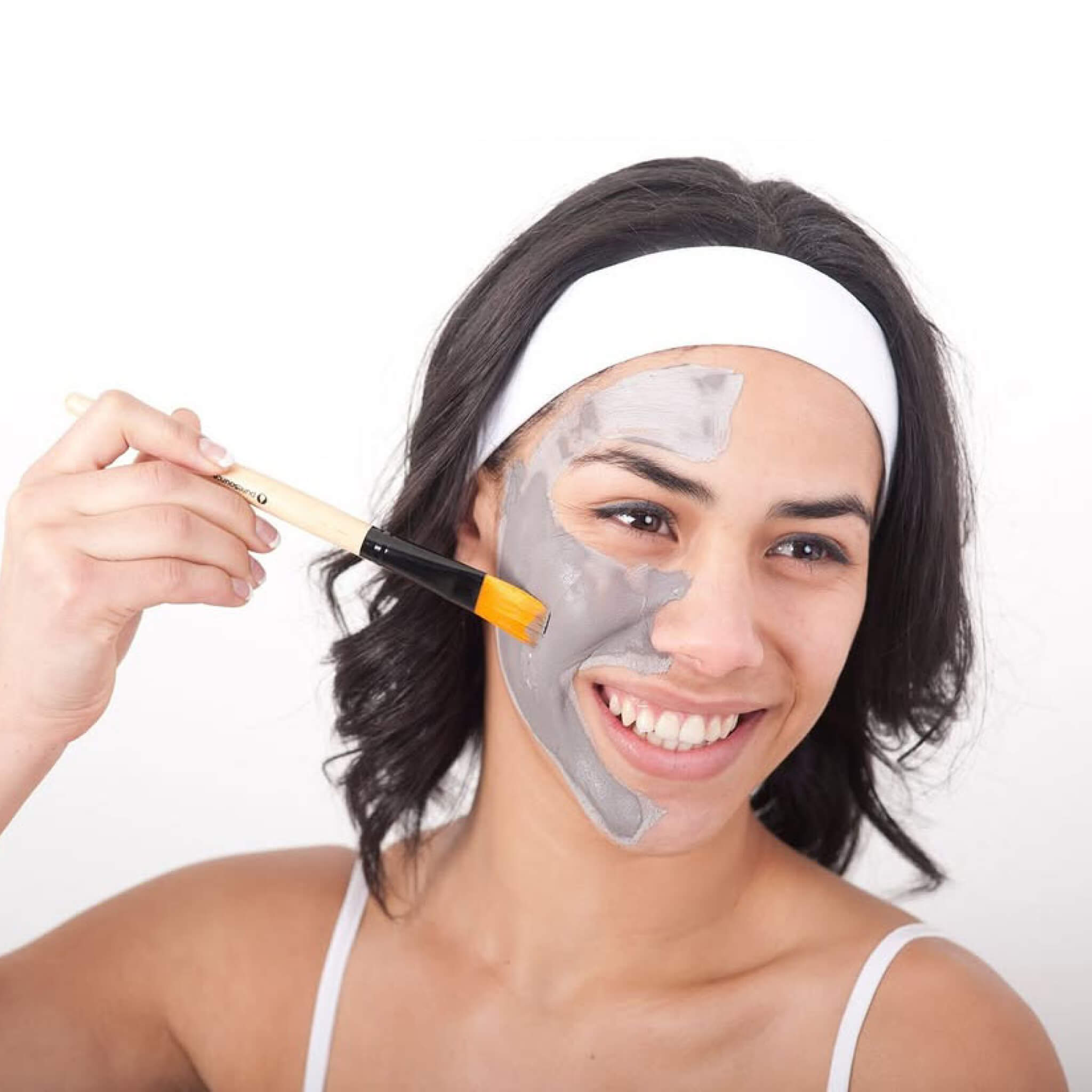 Woman applying a Puresource Rotorua Thermal mud mask with a brush on a white background