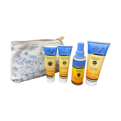 A skincare set from The Natural Land featuring Manusa Honey products, including a face cream, hand cream, and a bottle of honey spray, arranged next to a blue and white floral patterned zippered pouch on a white background.