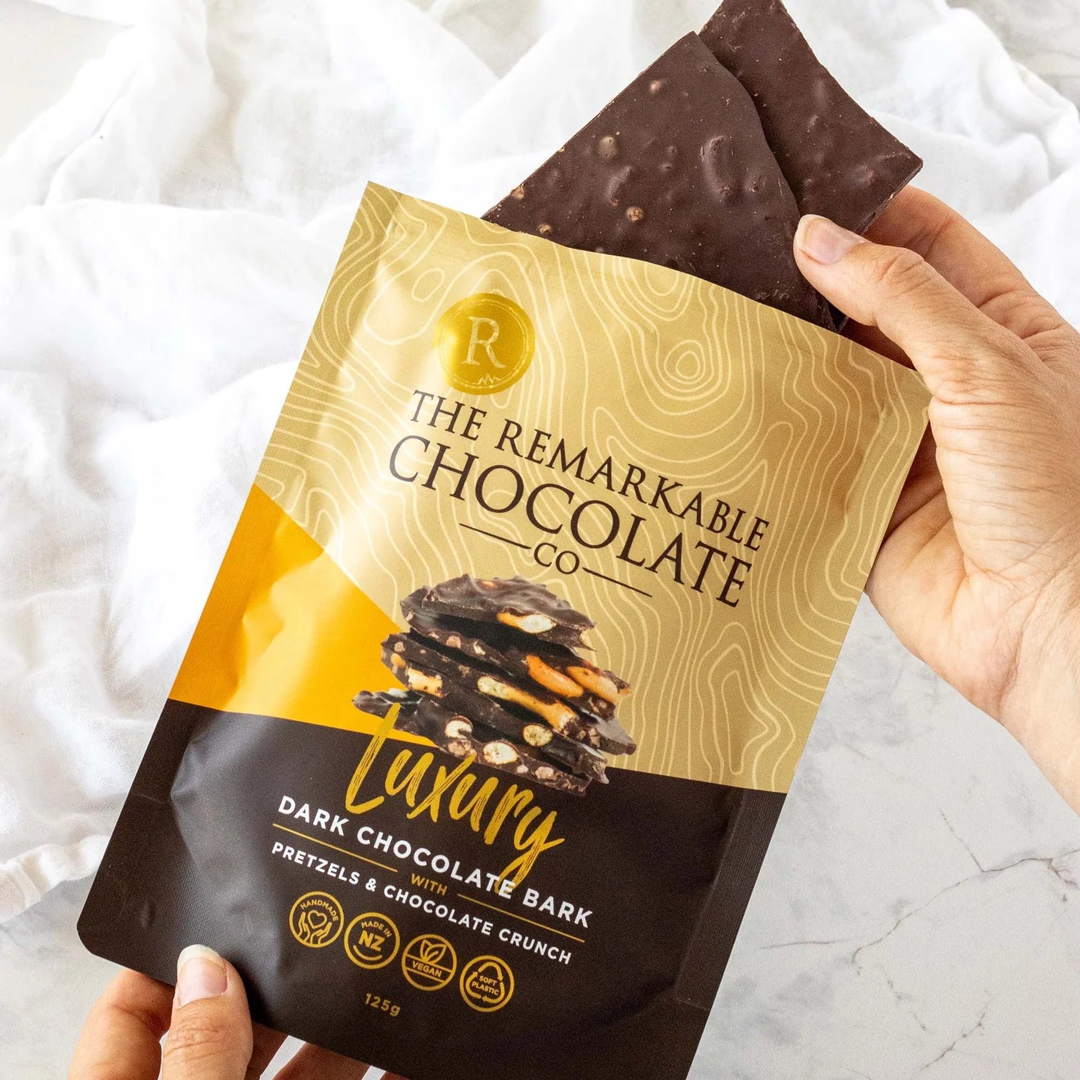 Hand holding a package of The Remarkable Chocolate Co. dark chocolate bark with pretzel and chocolate crunch