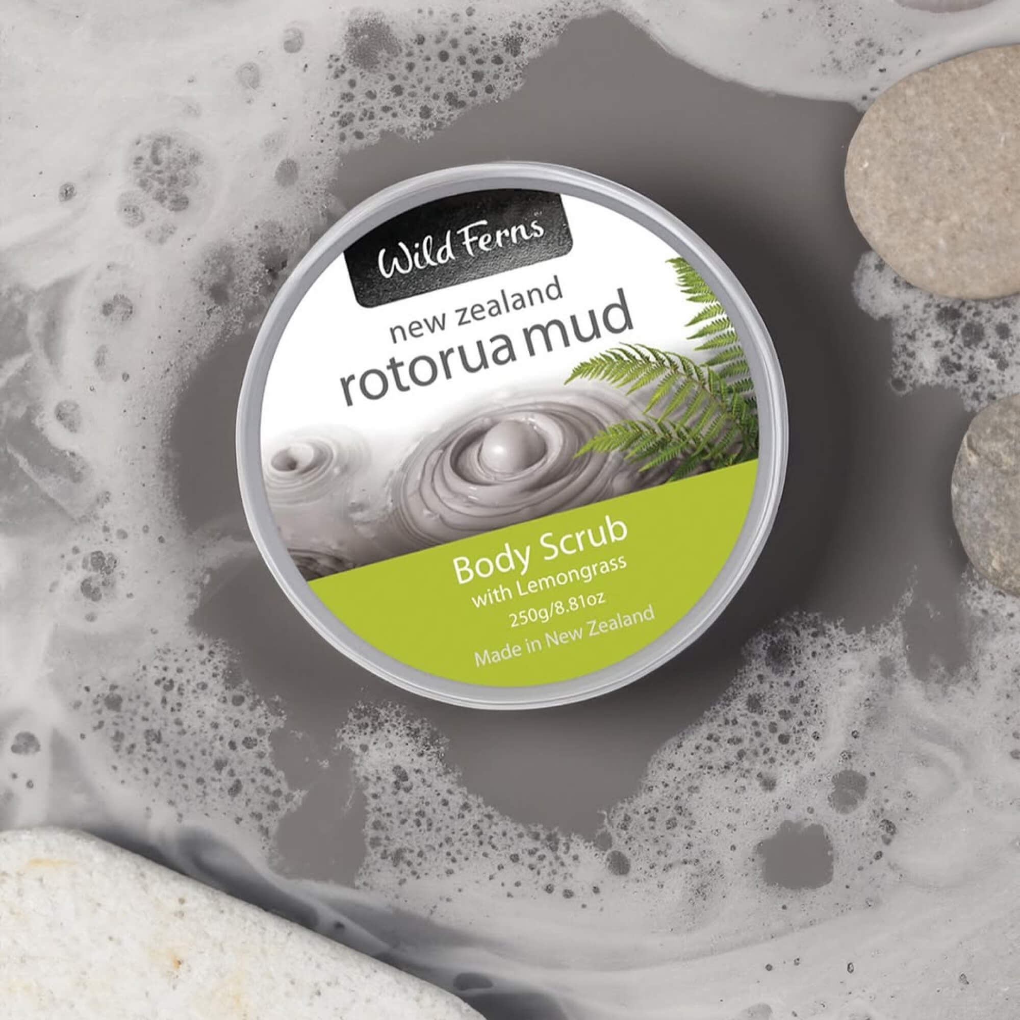 Wild Ferns Rotorua Mud Body Scrub container with foamy texture and stones in the background