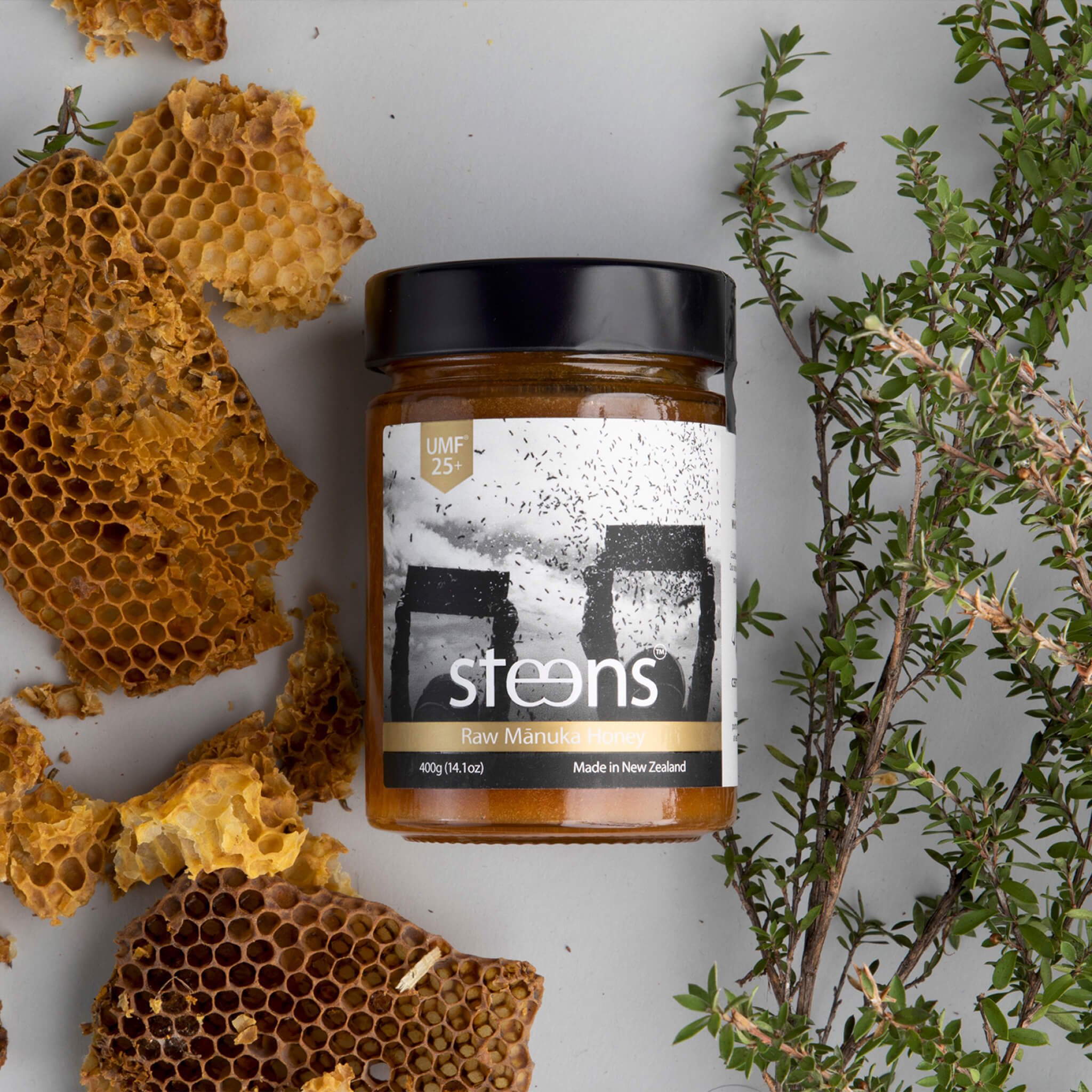 Jar of steens raw manuka honey with honeycomb and plants on a light background