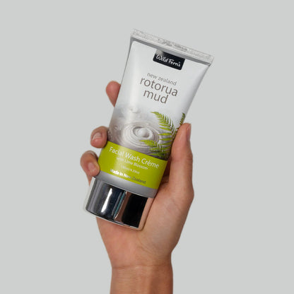 Hand holding a tube of Wild Ferns Rotorda Mud facial wash cream against a gray background